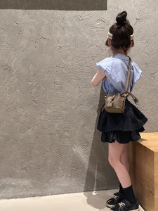 Girl's summer outfit detail with blue ruffle top and brown leather bucket crossbody bag