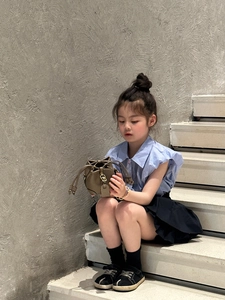 Toddler girl wearing a brown leather drawstring bucket bag on white stairs
