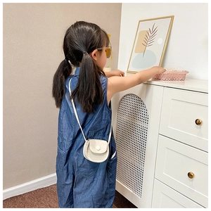 Detail of a mini cream white crossbody saddle bag with crocodile texture on a child model
