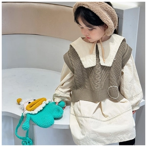 Détail d'un enfant portant robe crème, gilet en maille marron et sac au crochet vert