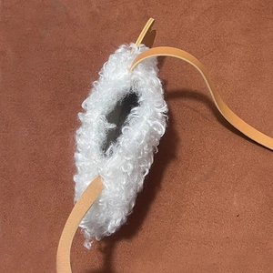 Gros plan sur la texture en laine d'agneau blanche et la bandoulière en cuir du sac enfant