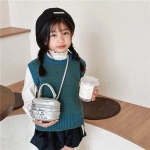 Girl wearing a silver quilted mini handbag with a knit vest and white lantern sleeve shirt