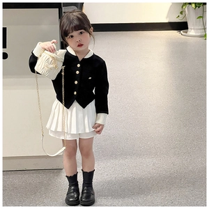 Detail of a girl wearing a black knit cardigan with gold buttons and a white pleated skirt