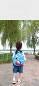 Toddler girl wearing a blue airplane hardshell backpack in a sunlit park setting