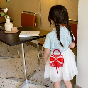 Mini sac fille en tweed rouge avec poignée perles et nœud, porté par un enfant