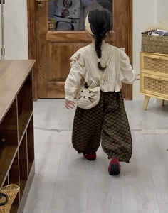 Back view of a child wearing a white cat crochet crossbody bag with a knit vest and floral pants