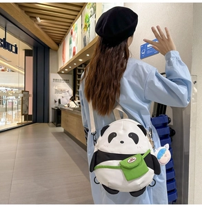 Detail of cute panda backpack with a green pocket and a cartoon charm on a canvas strap