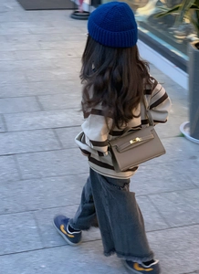 Detail of a child wearing a beige mini leather bag with metal clasp in an outdoor setting