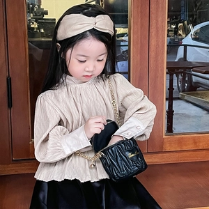 Mini girls' quilted bucket bag with golden chain and bow detail on beige outfit