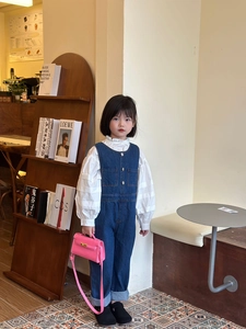 Detail of girls white ruffle blouse and blue denim overalls with a pink handbag