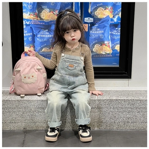 Kleinkind Mädchen mit rosa Schaf-Rucksack und Jeans-Latzhose in einer Alltagsszene