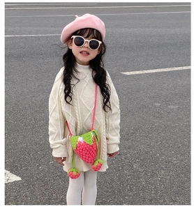 Detail of pink knitted strawberry crossbody bag with green leaf accent on a child model