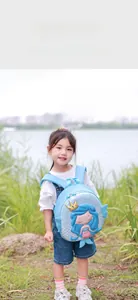 Toddler girl wearing light blue 3D mermaid backpack on grass in a park setting