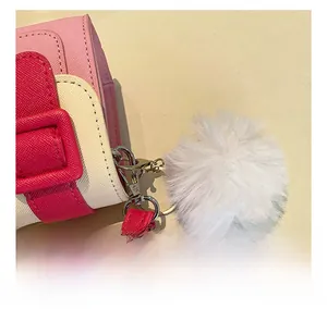 Détail du pompon blanc duveteux et de la texture du cuir Saffiano sur le sac à main