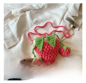 Close-up of strawberry-shaped crochet bag with green leaf details and hanging charms