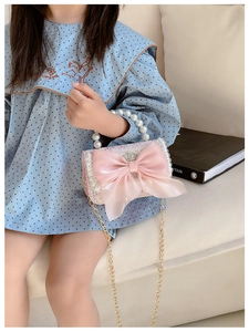 Detail of pink tweed girl's handbag with large mesh bow, pearl handle and gold chain strap