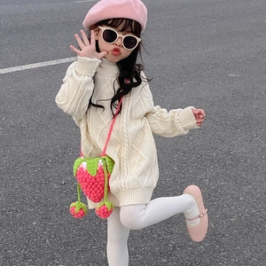Outdoor look of a child in cream cable-knit sweater with a crochet strawberry bag