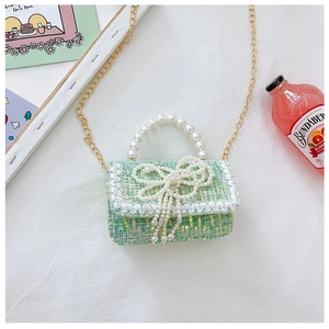 Close-up of green tweed bag with large pearl handle and bow detail on white table