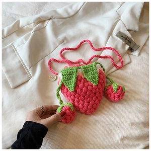 Detail of a handmade crochet strawberry bag featuring textured pink yarn and a slim strap