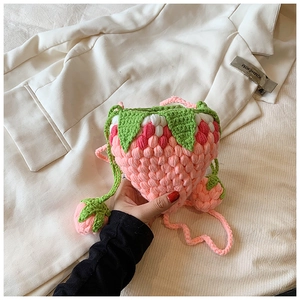 Detail of pink crochet strawberry shoulder bag with textured popcorn stitch and green leaves