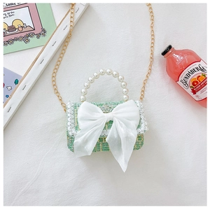 Detail of green tweed girls bag with white bow, pearl handle, and golden chain strap