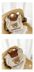 Close-up of beige canvas bag with cartoon bear embroidery and brown leather handle strap