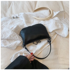 Detail of a minimalist black faux leather handbag with silver chain and zip closure