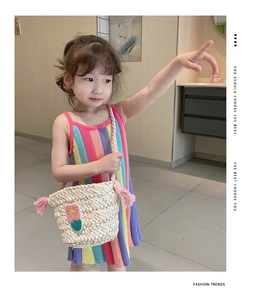 Detail of child's straw crossbody bag with pink floral appliqué and colorful knit dress