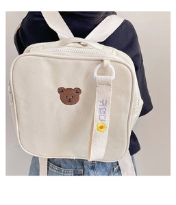 Détail de la broderie ours mignon et de l'étiquette fleur sur le sac à dos en toile