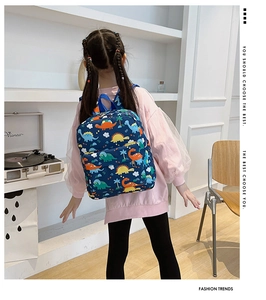 Rear view of a girl wearing a navy blue backpack with colorful dinosaur patterns in a room