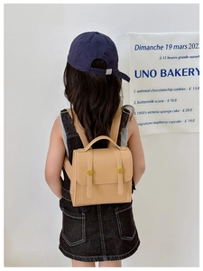 Rear view of a girl wearing a khaki PU leather vintage school backpack in a cozy room
