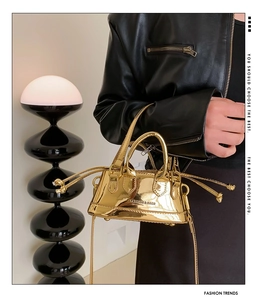 Close-up of metallic gold mini shell bag with glossy finish and decorative drawstrings