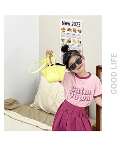 Detail showing a girl wearing a pink logo T-shirt and a purple pleated skirt with a yellow bag