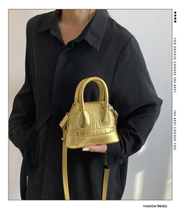 Detail of a golden mini shell bag with crocodile texture and metallic top handles