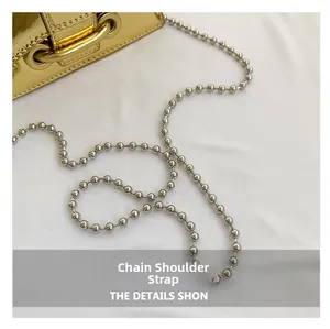Detailed view of silver bead chain strap on a glossy metallic gold mini shoulder bag