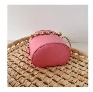 Mini sac seau rose avec chaîne à billes dorée présenté dans un panier en paille tressée