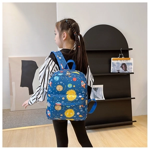 Detail view of child wearing a blue space-themed backpack with cartoon rocket and planet prints