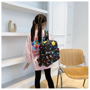 Child wearing a black backpack with space cartoon prints including rockets and planets