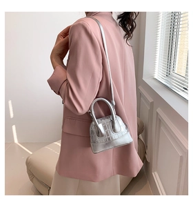 Detail of silver shell-shaped shoulder bag with crocodile texture worn by a model