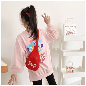 Close-up of red canvas kids chest bag featuring white Sup lettering with adjustable strap
