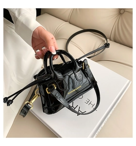 Close-up of black patent leather mini shell bag with gold hardware and logo detail