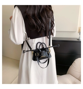 Model wearing a mini black patent leather shell bag with drawstrings and mirror finish