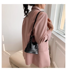 Detail of black mini shell crossbody bag with crocodile pattern on a pink suit model
