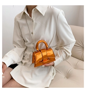 Detail of glossy orange mini handbag with metal chain strap and sleek mirror finish