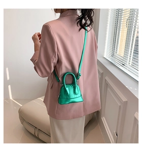 Close-up of vibrant green crocodile-embossed mini shell bag worn on a pink blazer