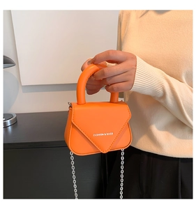 Detail einer hellorangen Mini-Handtasche mit weißem Text und silbernem Kettenriemen