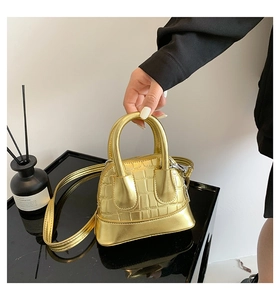 Detail of mini gold shell bag with crocodile embossed texture and metallic finish handle