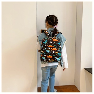 Toddler wearing a cartoon dinosaur backpack with adjustable straps on a white background