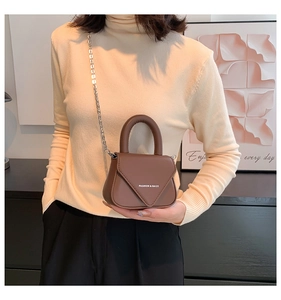 Detailansicht der braunen Mini-Umhängetasche aus Leder mit silberner Kette am Pullover