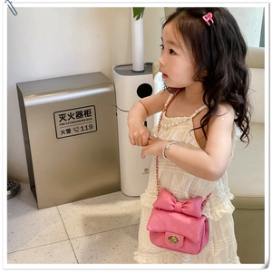 Detail of pink quilted girl's crossbody bag featuring a large bow and metal chain strap